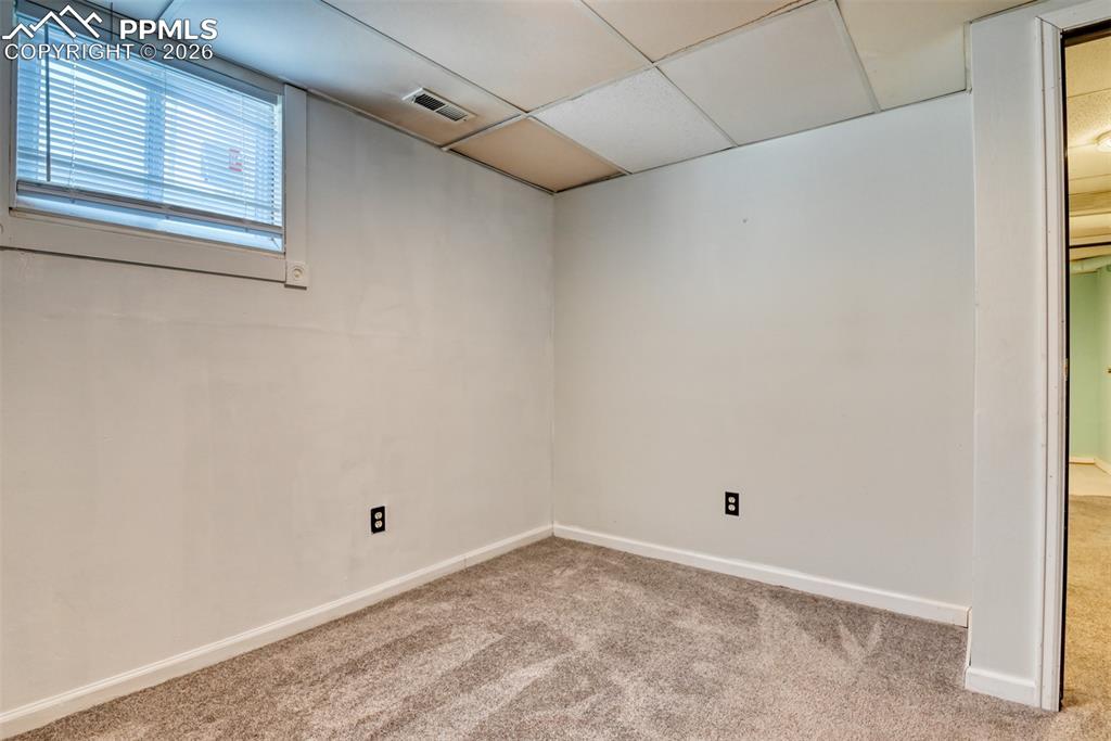 Carpeted spare room with visible vents, baseboards, and a drop ceiling