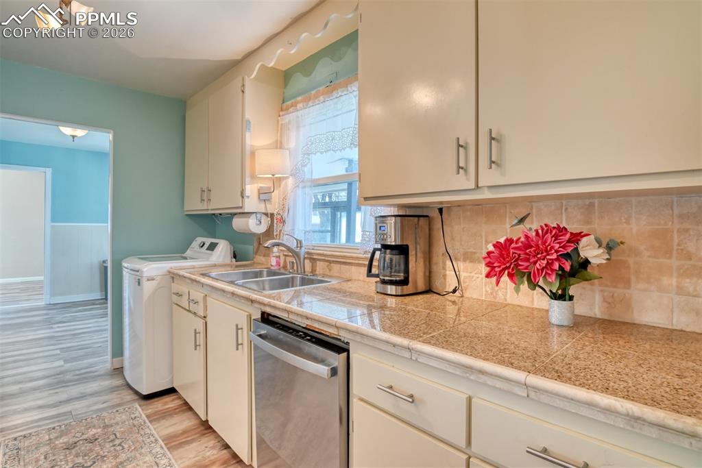 Primary Kitchen with light wood-style flooring, a sink, stainless steel dishwasher, tile counters, and washer and clothes dryer