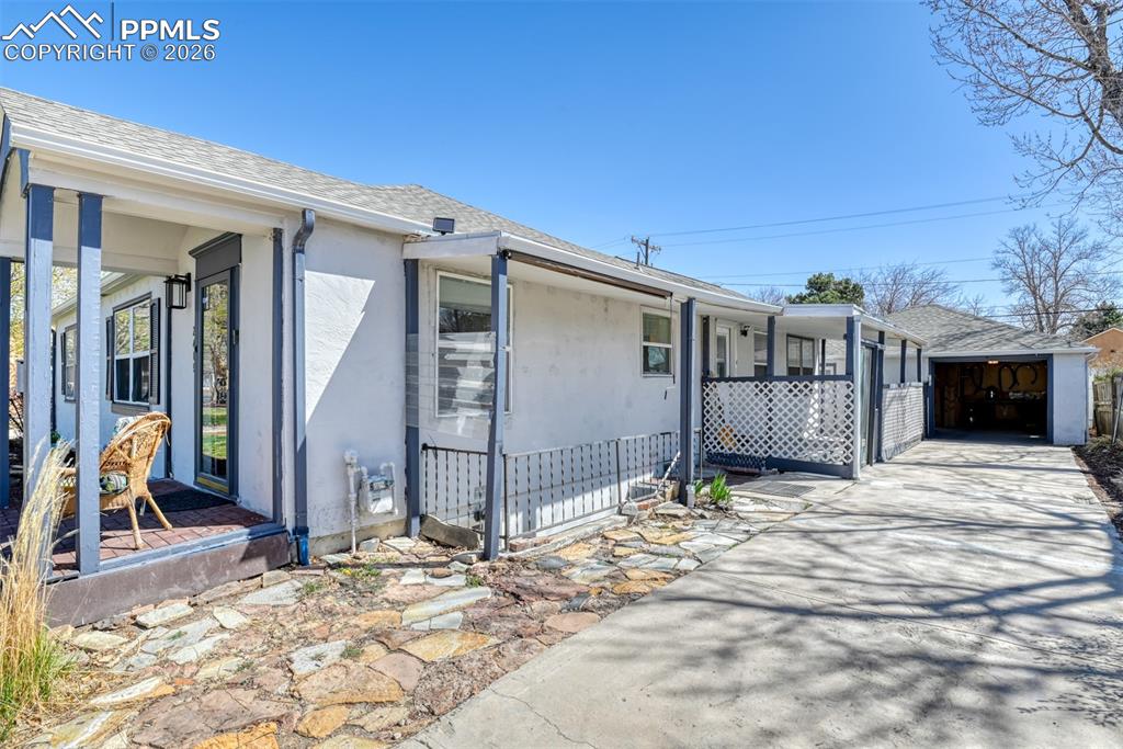 View of side of property with concrete driveway, roof with shingles, covered porch, and stucco siding