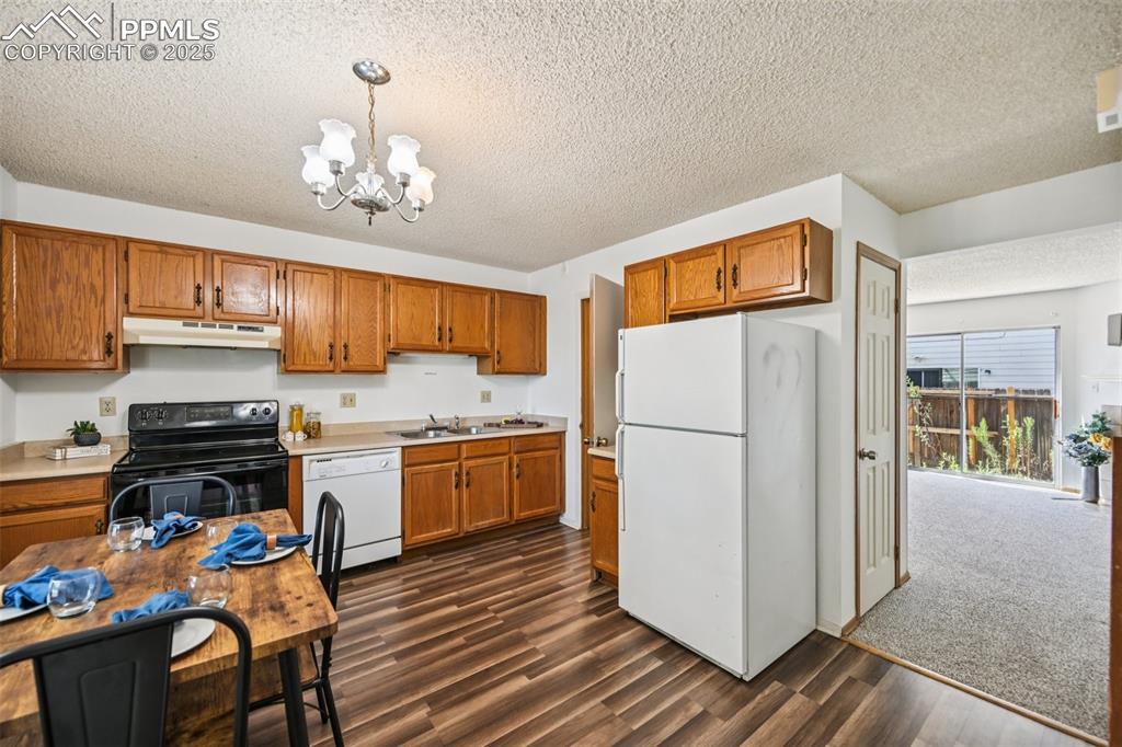Kitchen with white appliances, brown cabinetry, decorative light fixtures, a chandelier, and a textured ceiling