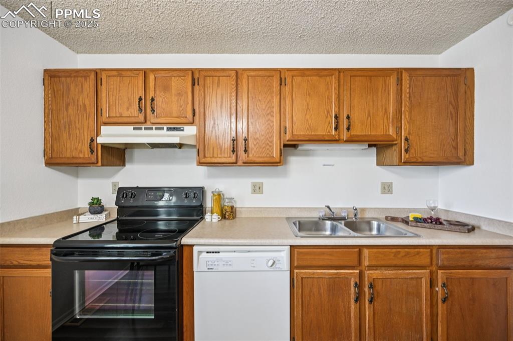 Kitchen featuring black range with electric cooktop, brown cabinetry, dishwasher, light countertops, and a textured ceiling