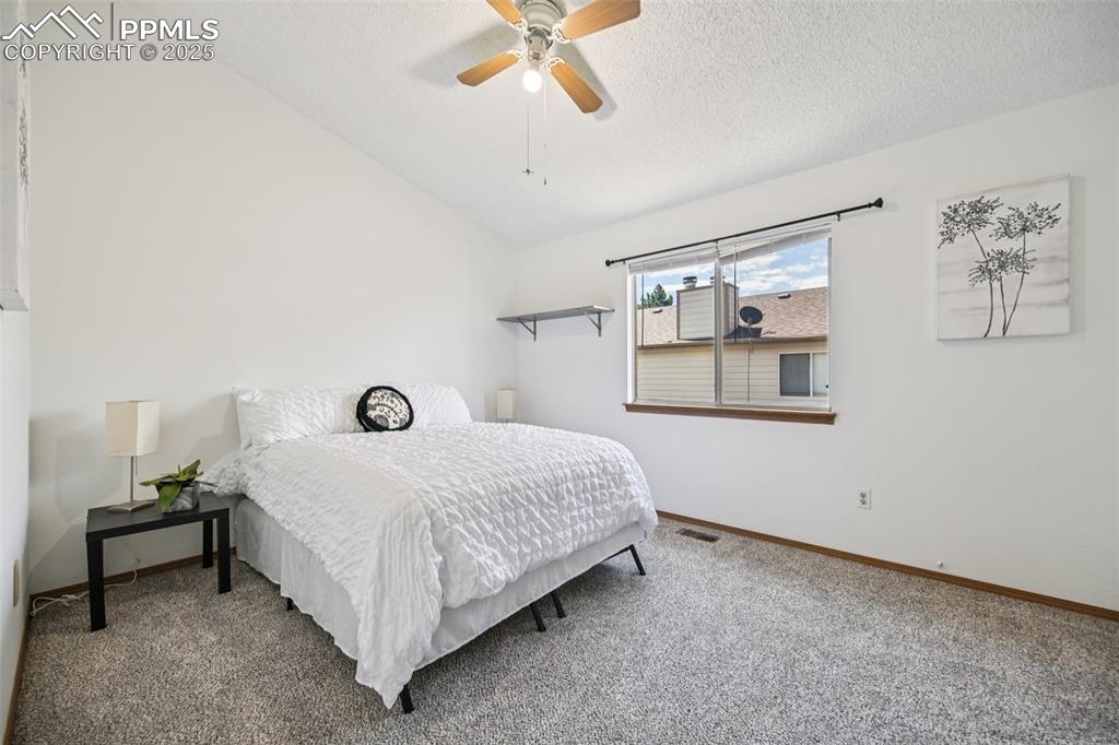 Bedroom featuring lofted ceiling, carpet, a ceiling fan, and a textured ceiling