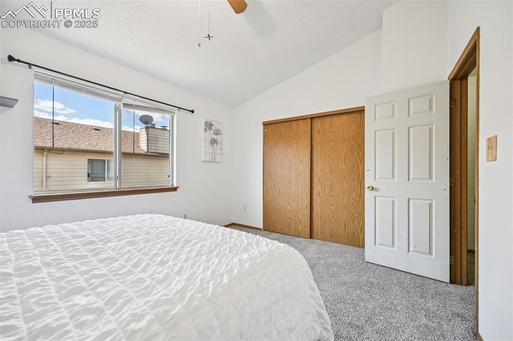 Carpeted bedroom with vaulted ceiling, a closet, ceiling fan, and a textured ceiling