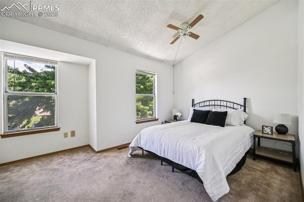 Bedroom featuring vaulted ceiling, a textured ceiling, carpet floors, and ceiling fan