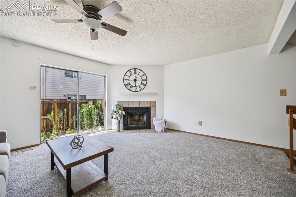 Carpeted living room featuring a tile fireplace, a textured ceiling, and ceiling fan