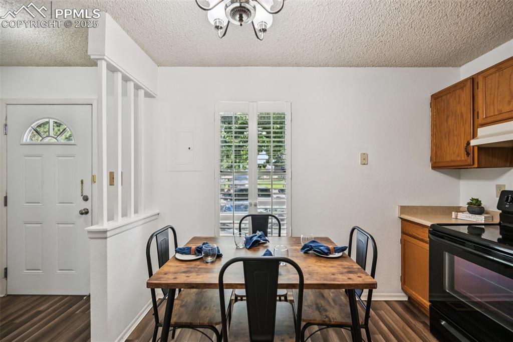 Dining room with healthy amount of natural light, a textured ceiling, dark wood-type flooring, and a chandelier