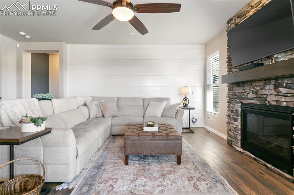 Living room with wood finished floors, a fireplace, ceiling fan, and wooden walls