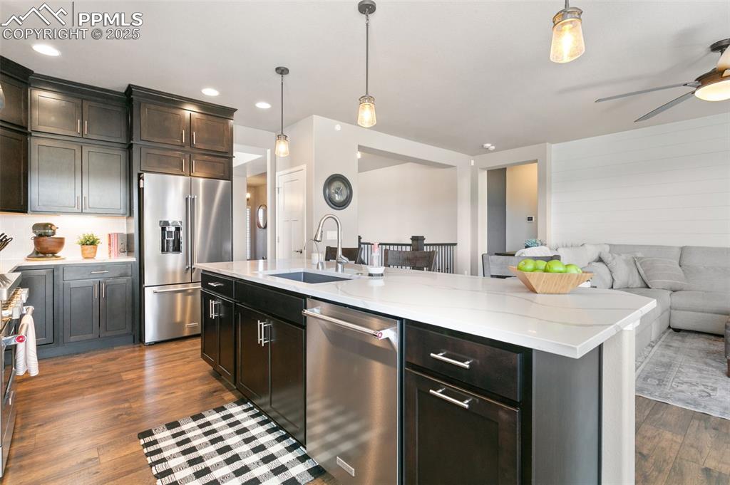Kitchen with open floor plan, stainless steel appliances, hanging light fixtures, light stone countertops, and dark wood-type flooring