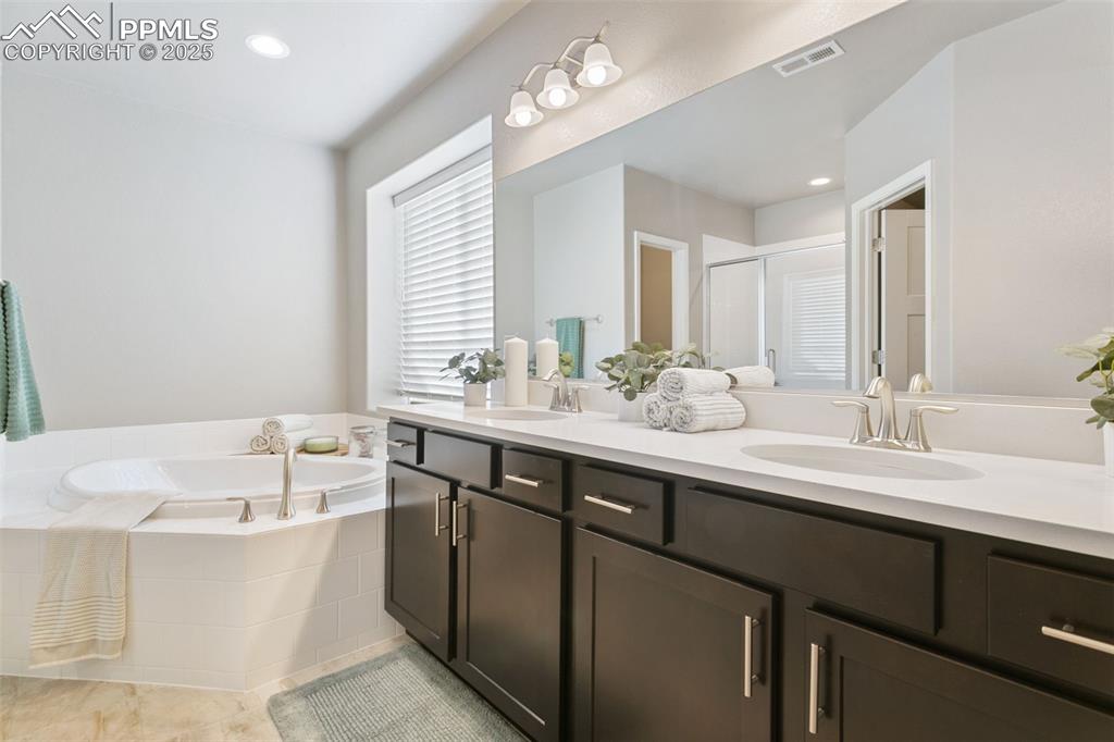 Bathroom featuring a stall shower, recessed lighting, a bath, double vanity, and light tile patterned flooring