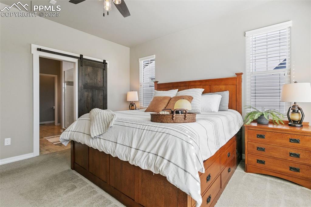 Bedroom featuring a barn door, light carpet, connected bathroom, and ceiling fan