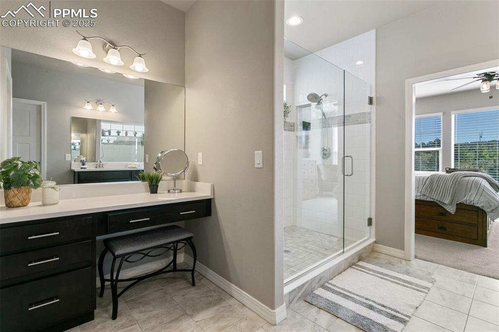Ensuite bathroom featuring a shower stall, vanity, ceiling fan, and light tile patterned floors