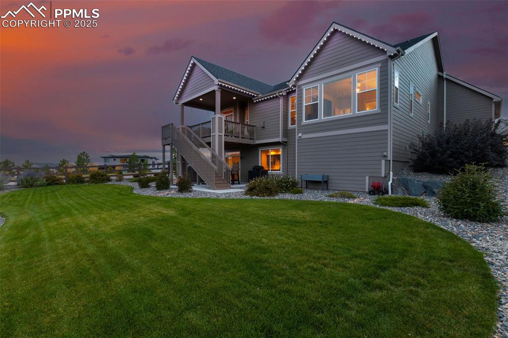 Back of property at dusk featuring a patio, a lawn, stairs, and a deck