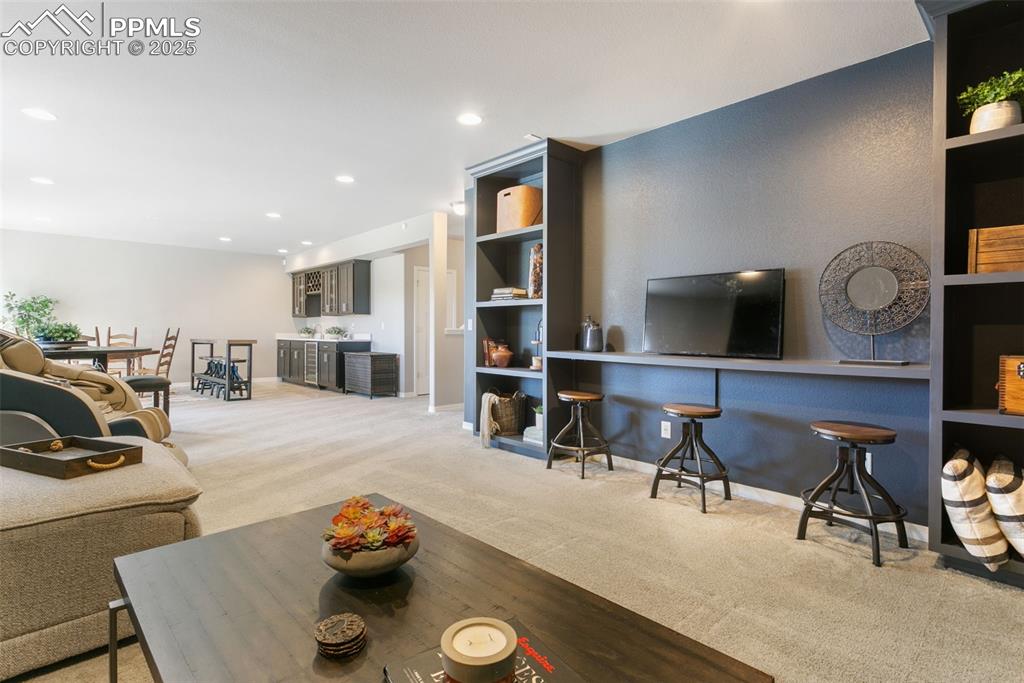Living room with light colored carpet, recessed lighting, and bar