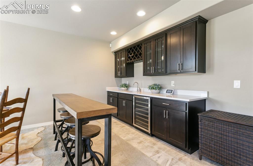 Indoor wet bar with glass insert cabinets, recessed lighting, beverage cooler, and dark cabinets