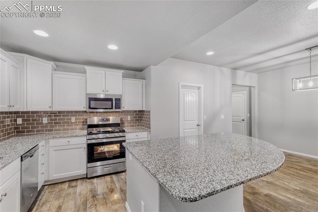 Kitchen featuring stainless steel appliances, a kitchen island, LVP flooring, and white cabinetry