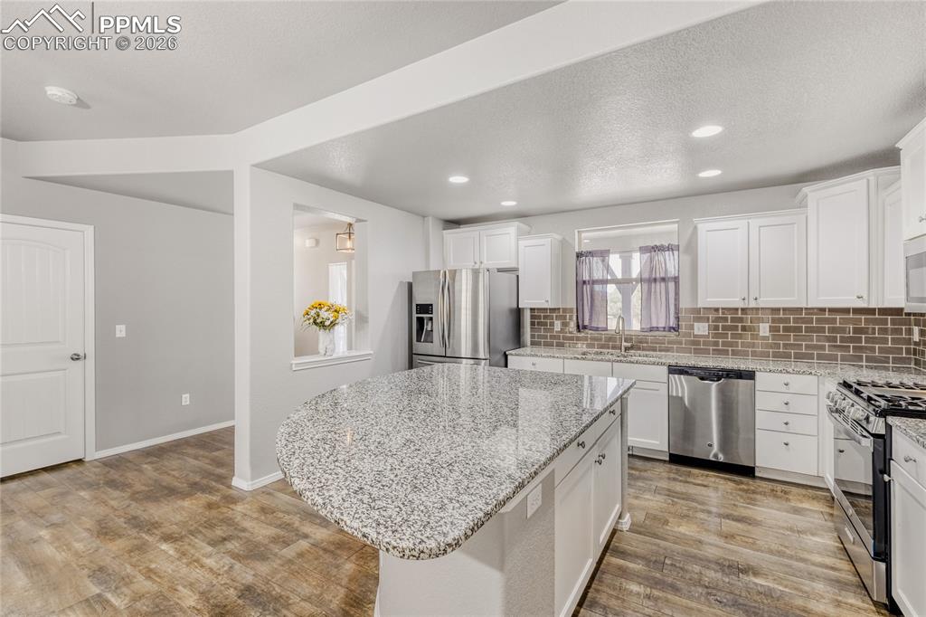 Kitchen with backsplash, white cabinets, stainless steel appliances, LVP flooring, and light granite countertops