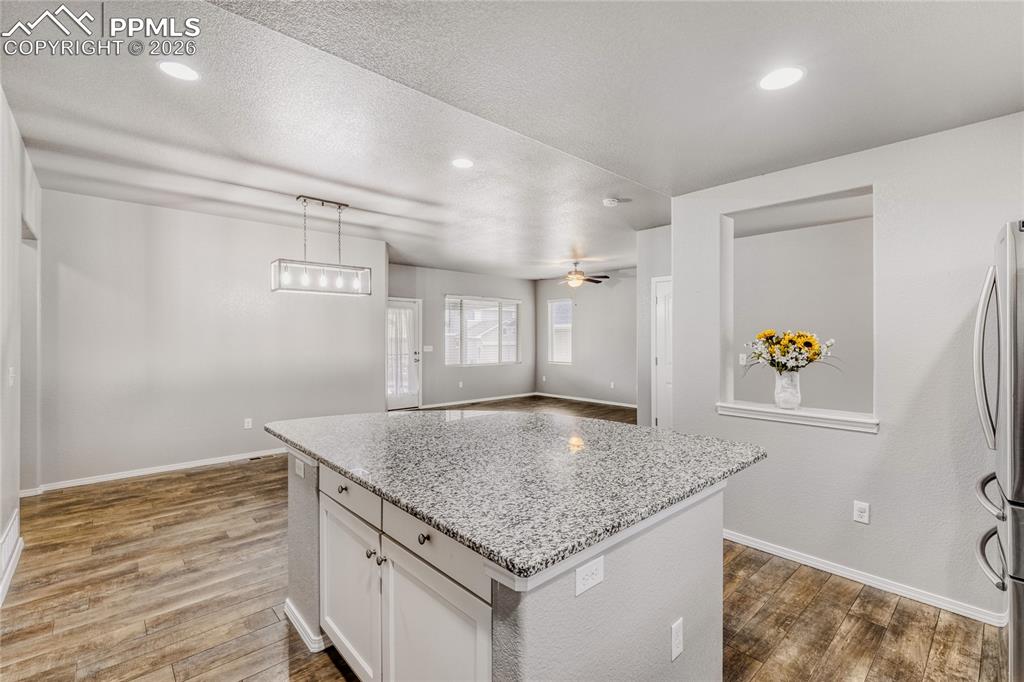 Kitchen with LVP flooring, light granite counters, white cabinetry, a kitchen island, and decorative light fixture