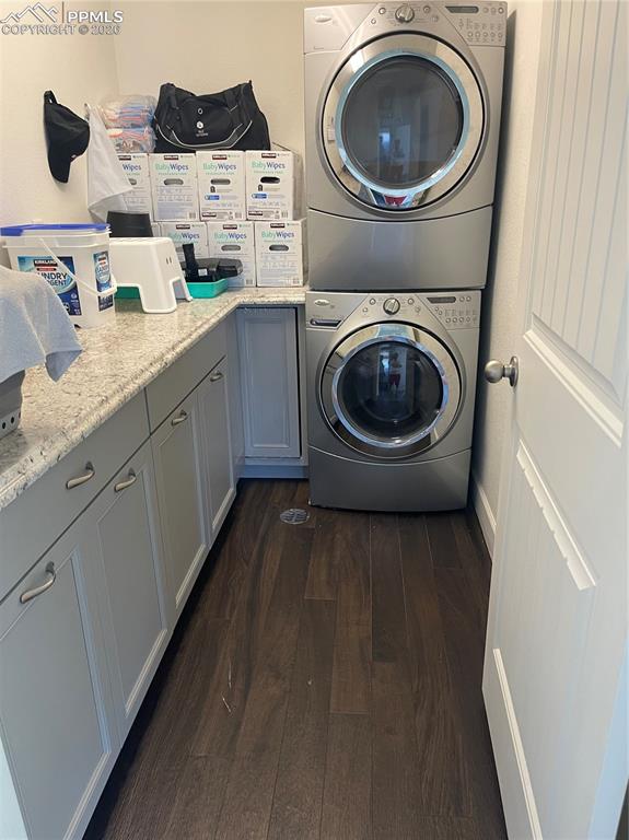 Laundry area featuring stacked washer / drying machine, dark wood-style floors, and cabinet space