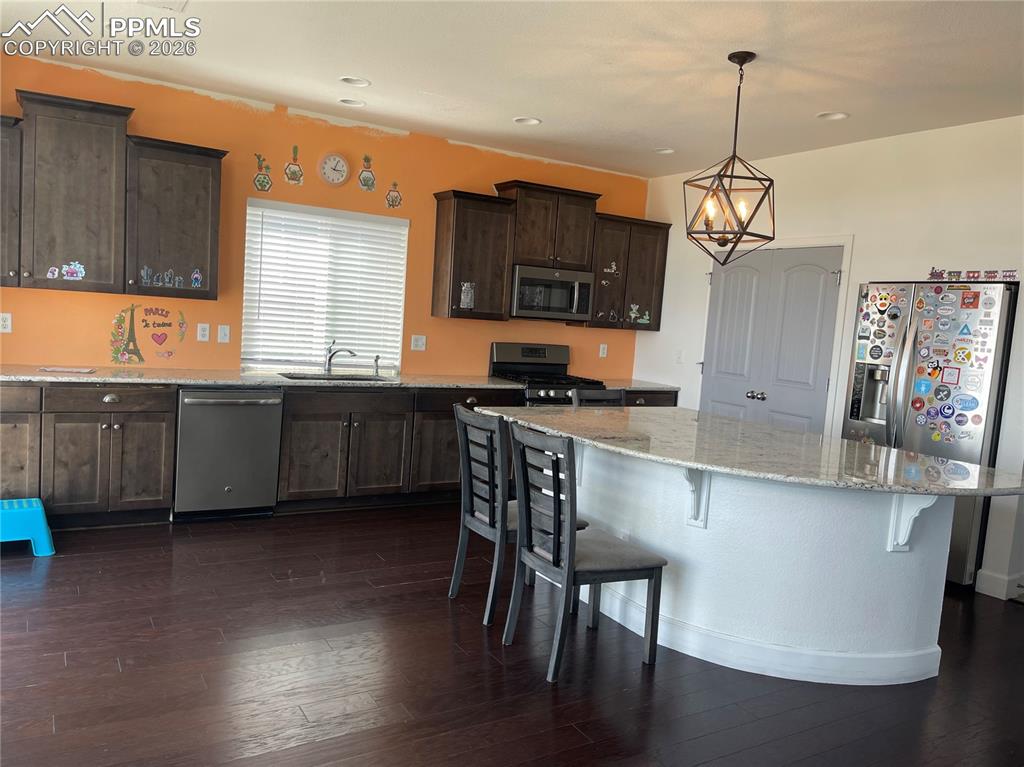 Kitchen with dark wood finish cabinetry, stainless steel appliances, a kitchen breakfast bar, light stone countertops, and dark wood-type flooring