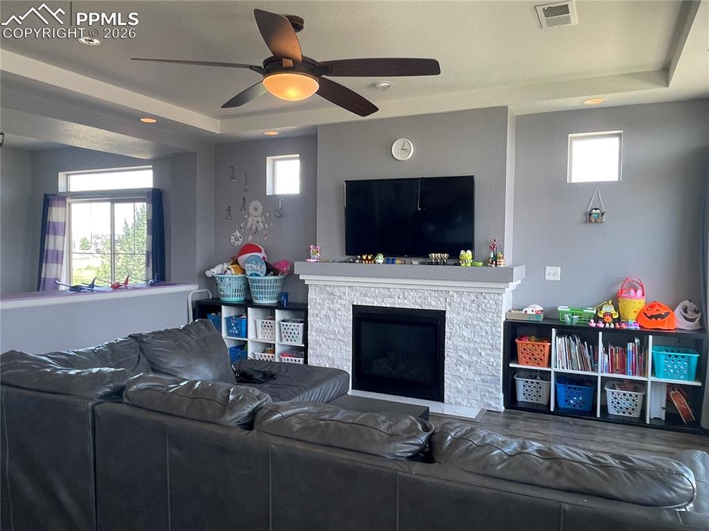 Living room with ceiling fan, healthy amount of natural light, a raised ceiling, a fireplace, and recessed lighting