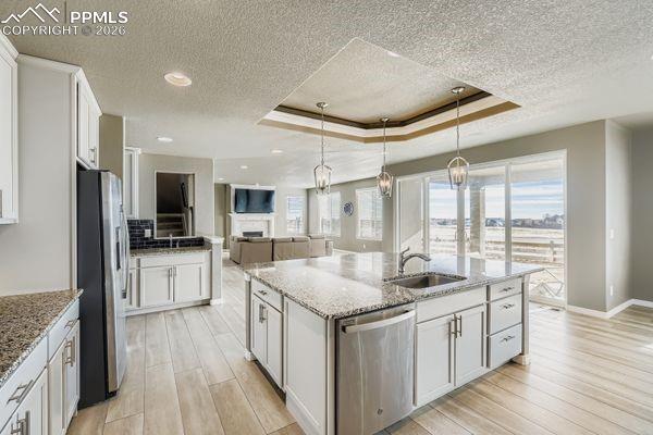 Kitchen featuring a tray ceiling, white cabinetry, open floor plan, light stone counters, and a textured ceiling
