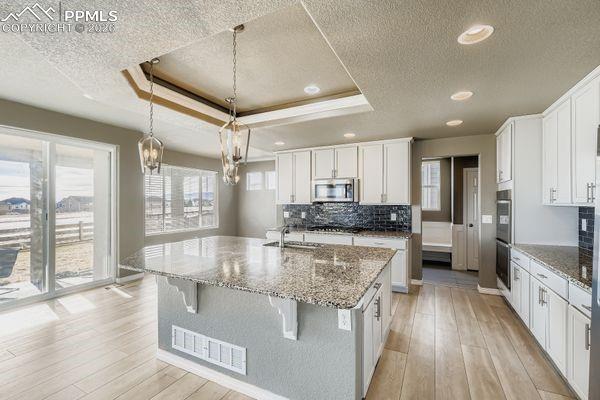 Kitchen featuring white cabinetry, light stone counters, light wood-style floors, a textured ceiling, and a kitchen island with sink