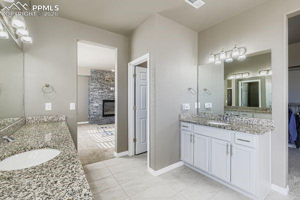 Bathroom with a fireplace, two vanities, a spacious closet, light tile patterned flooring, and light colored carpet