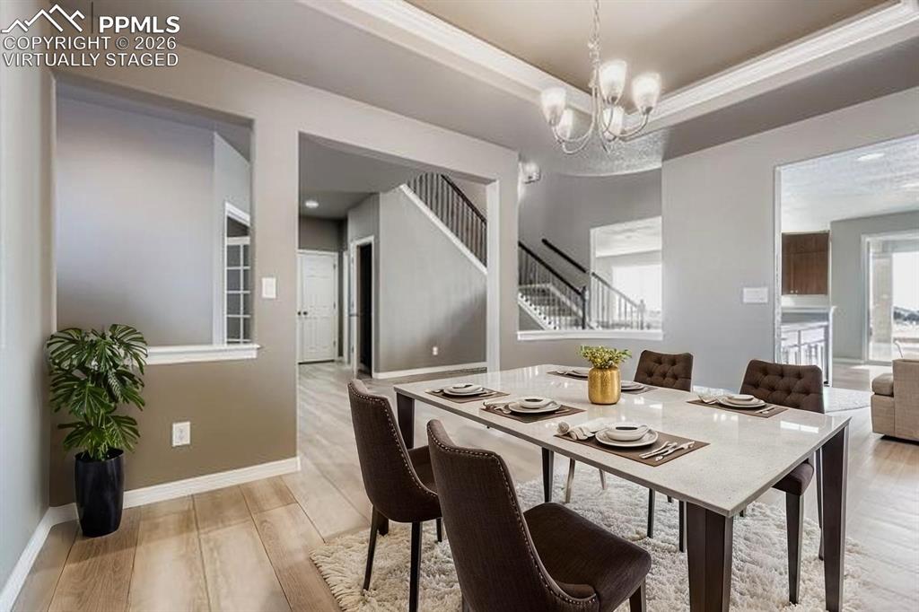 Virtually staged dining room with light wood-style flooring, stairway, a tray ceiling, and a chandelier