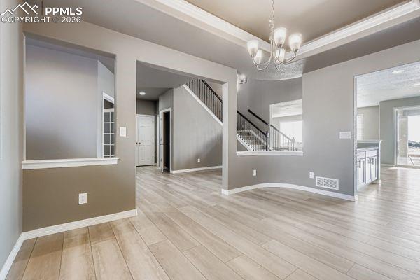 Unfurnished room with a chandelier, light wood-style flooring, a raised ceiling, and stairs