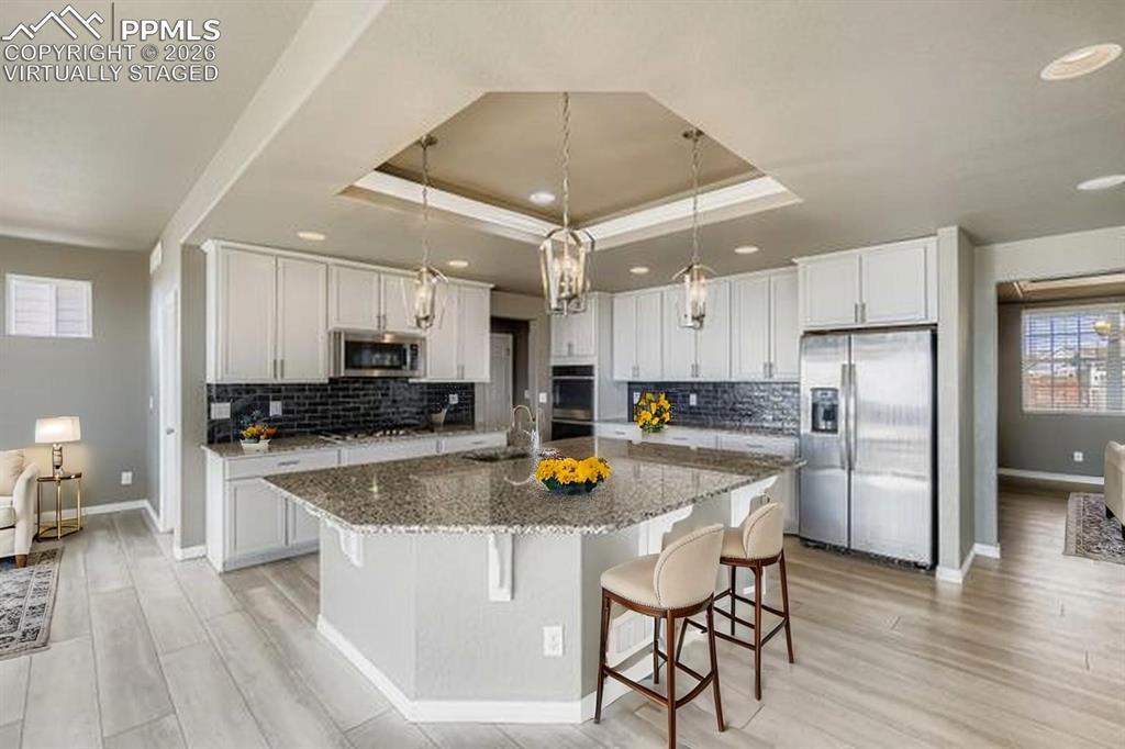 Virtually staged kitchen featuring stainless steel appliances, light wood-type flooring, a breakfast bar area, white cabinetry, and recessed lighting