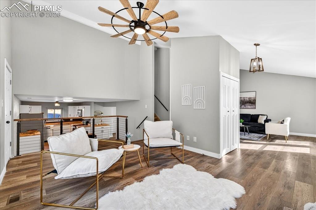 Sitting room with a ceiling fan, wood finished floors, a high ceiling, and an upstairs landing