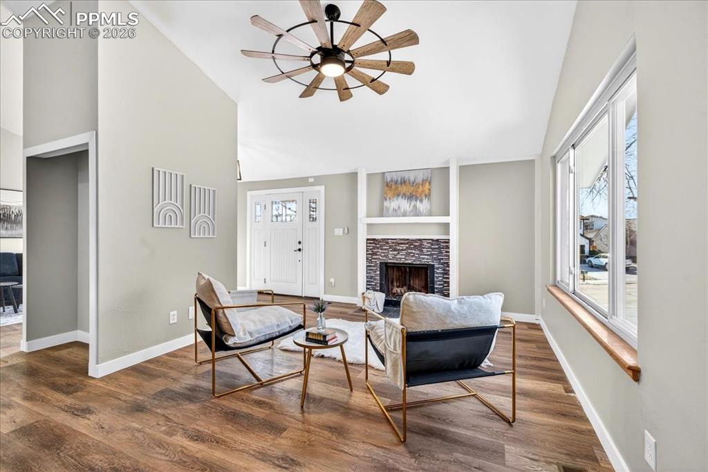 Living room with a fireplace, wood finished floors, a ceiling fan, healthy amount of natural light, and lofted ceiling