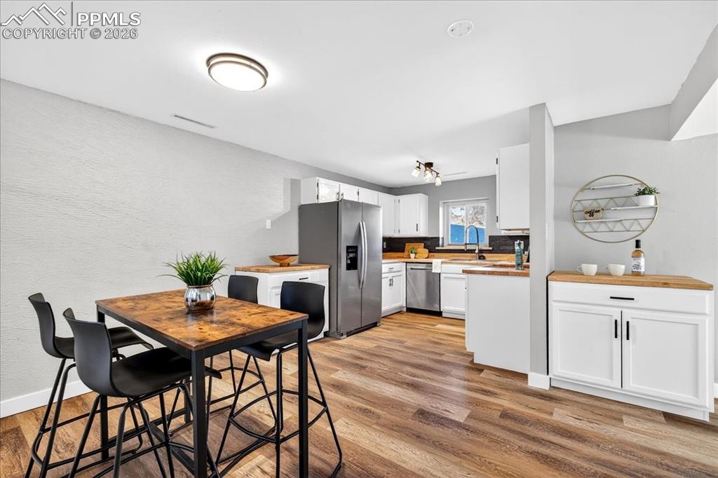 Kitchen with stainless steel appliances, white cabinets, light wood-style floors, a textured wall, and butcher block countertops