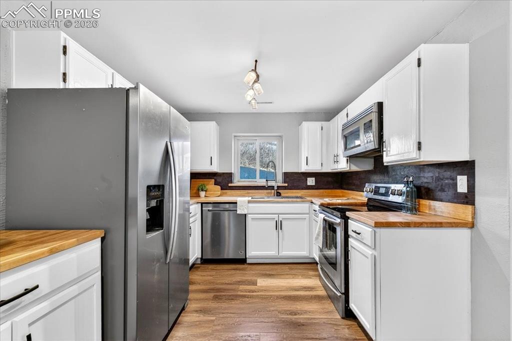 Kitchen with butcher block counters, stainless steel appliances, white cabinets, and dark wood-type flooring