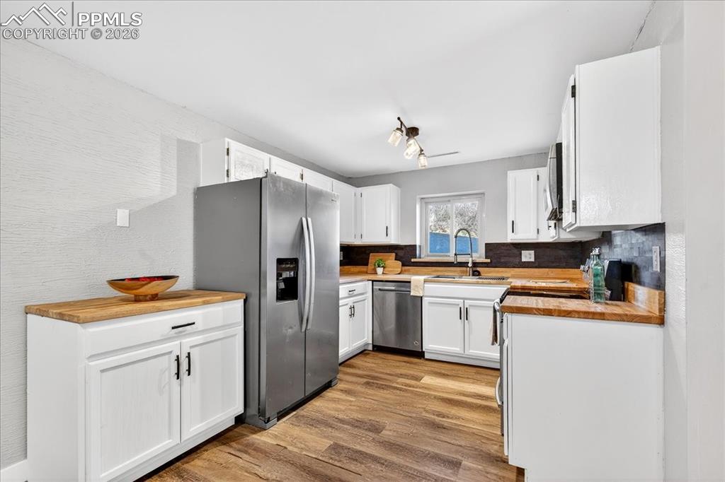 Kitchen with stainless steel appliances, wood counters, white cabinetry, light wood-style flooring, and a textured wall