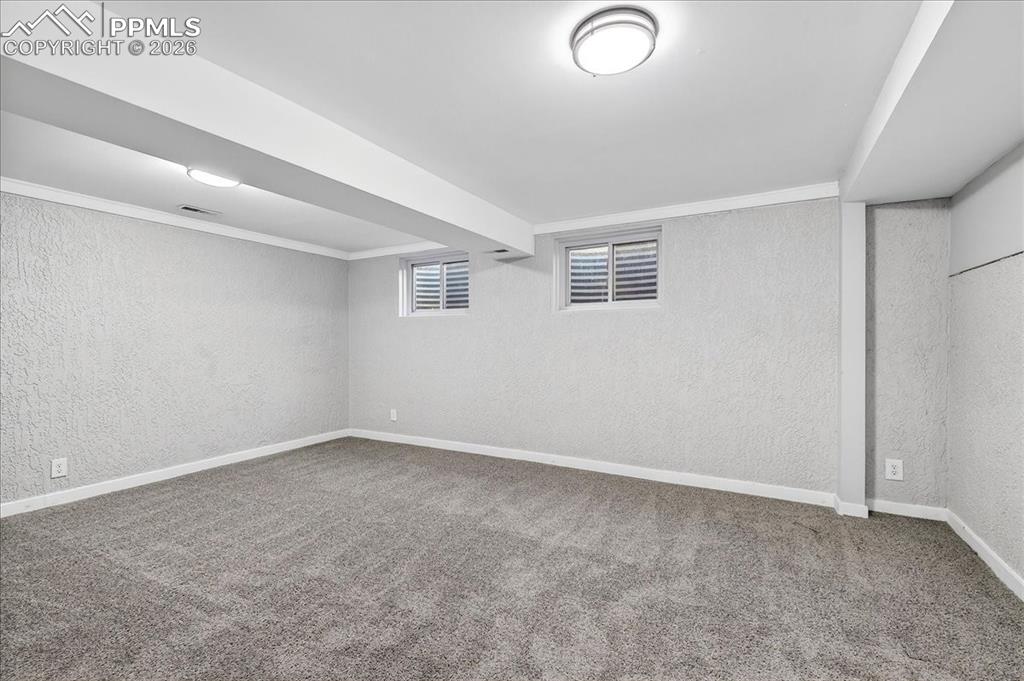 Below grade area with a textured wall, carpet flooring, and ornamental molding