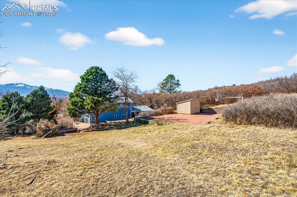 View of grassy yard with a patio, a storage shed, and a mountain view