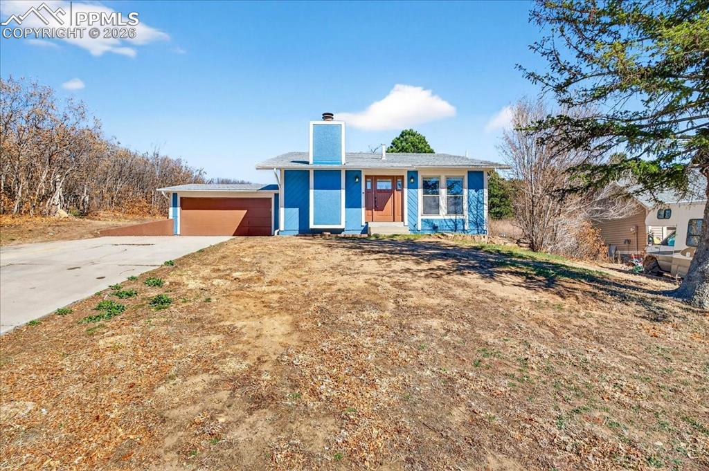 View of front facade featuring a chimney and concrete driveway