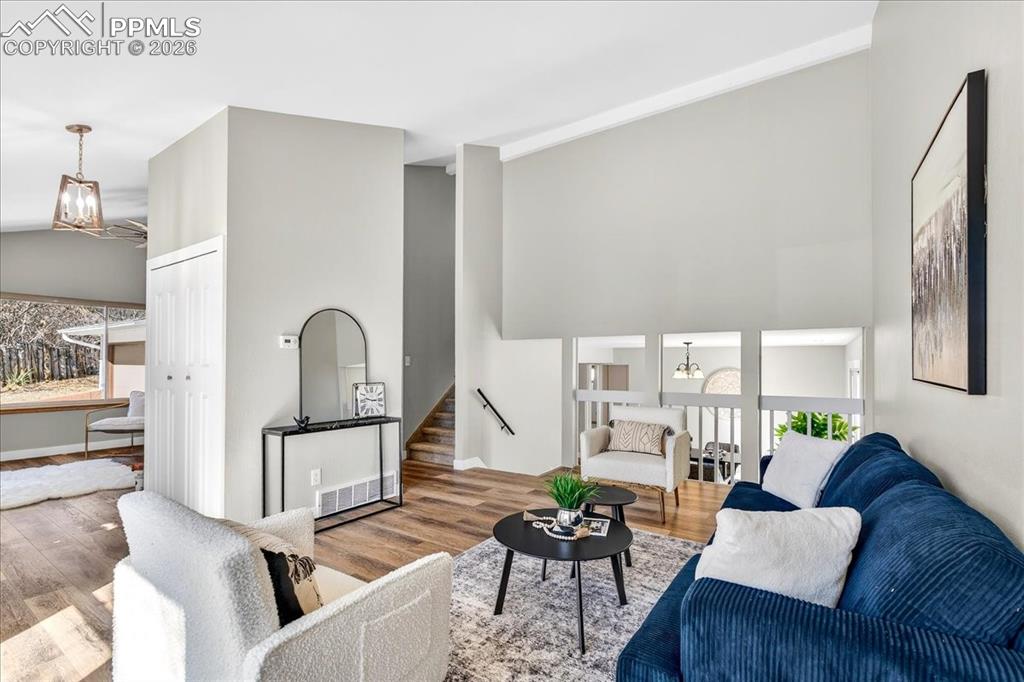 Living room with hanging lights, wood finished floors, and a high ceiling