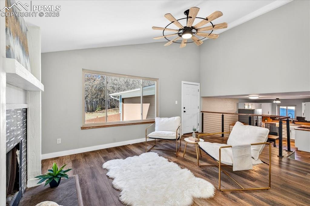 Sitting room with a fireplace, ceiling fan, wood finished floors, and vaulted ceiling