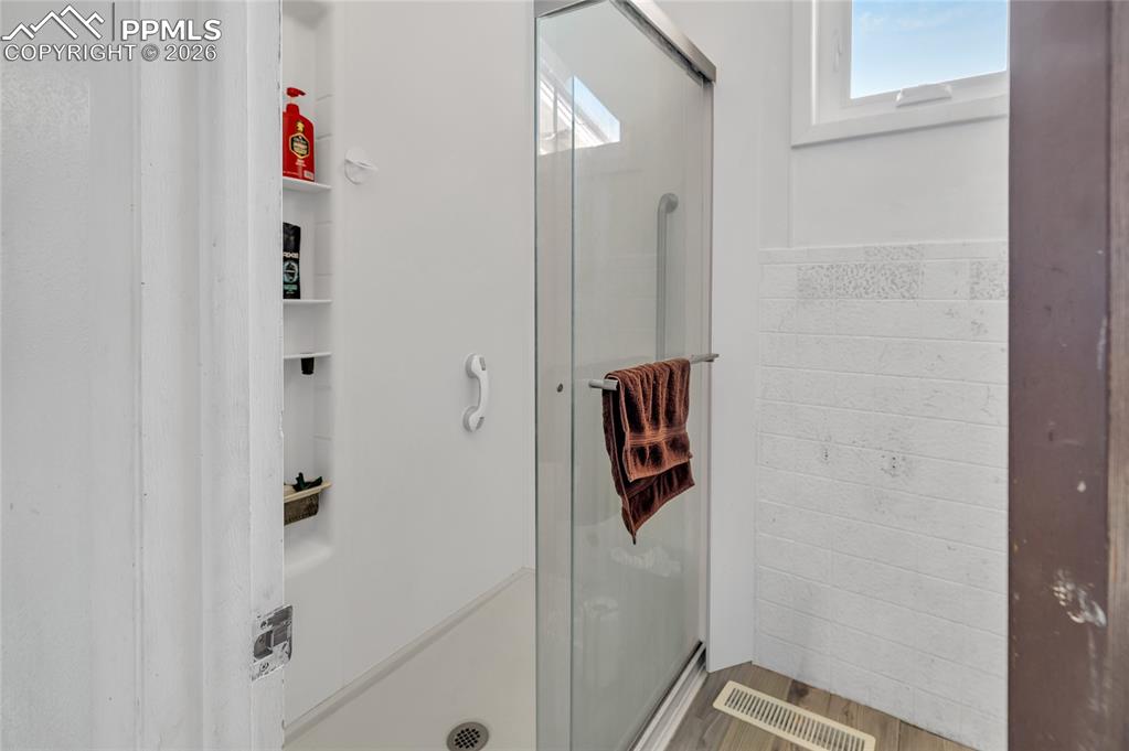 Full bath featuring a stall shower, tile walls, wainscoting, and light wood finished floors