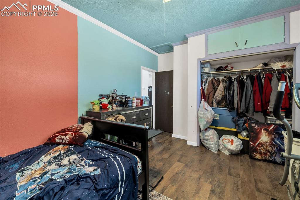 Bedroom with dark wood-style floors, a textured ceiling, a closet, and crown molding