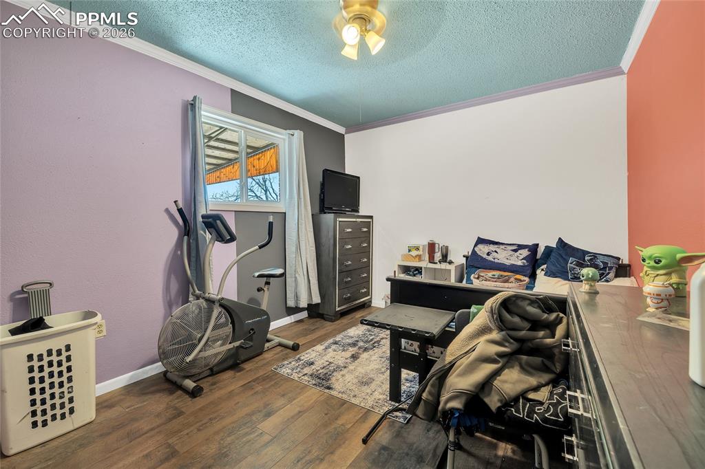 Exercise area with dark wood-style flooring, a textured ceiling, ornamental molding, and ceiling fan