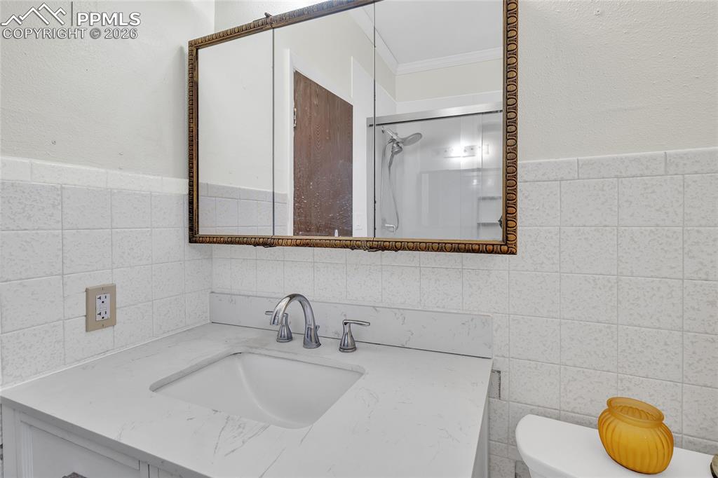 Bathroom featuring vanity, a shower, crown molding, and tile walls
