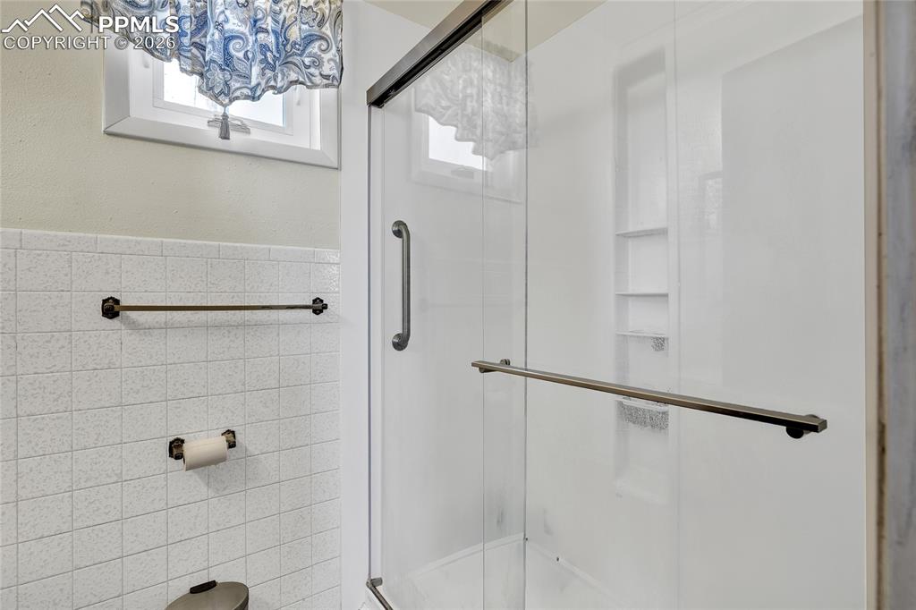 Full bathroom with tile walls, a shower stall, and wainscoting