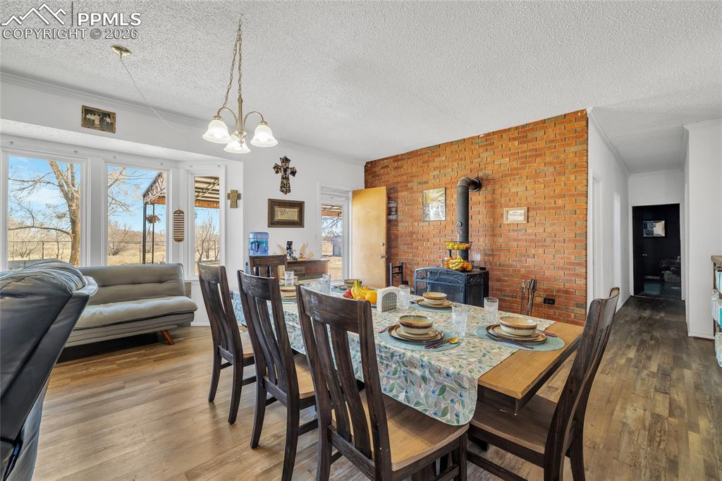 Dining area featuring a wood stove, hardwood / wood-style floors, a textured ceiling, hanging lights, and brick wall