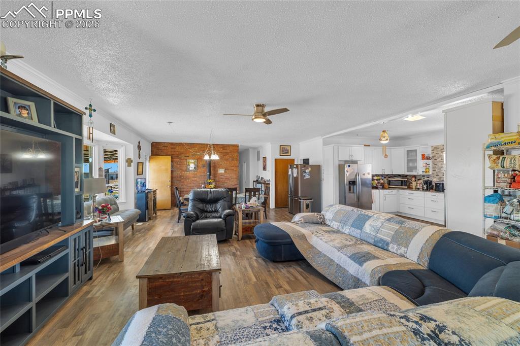 Living room with ceiling fan, dark wood-style flooring, a textured ceiling, and brick wall
