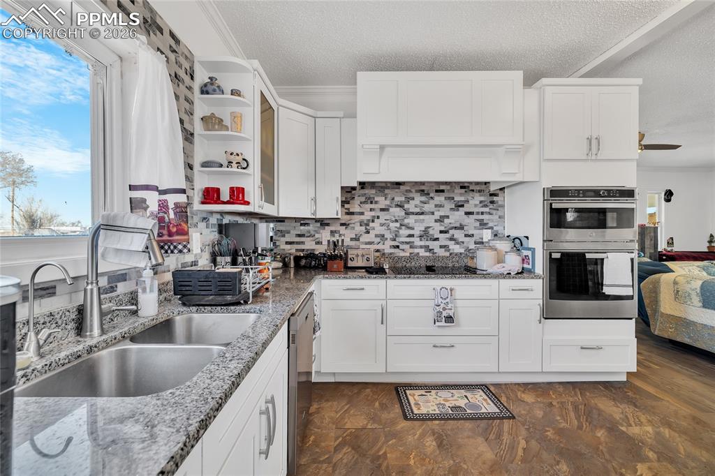 Kitchen with white cabinets, open shelves, stainless steel appliances, light stone countertops, and a textured ceiling
