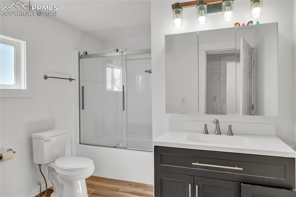 ADU Bathroom with vanity, shower / bath combination with glass door, light wood-type flooring, and a textured ceiling