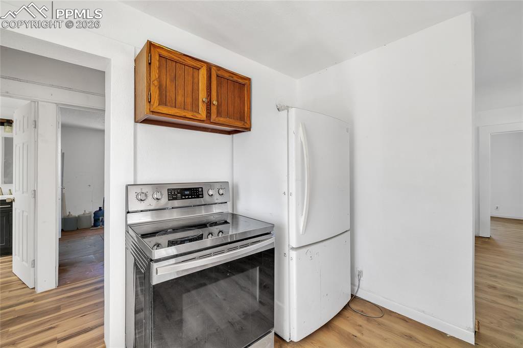 ADU Kitchen with stainless steel range with electric stovetop, wood finish cabinetry, light wood-style flooring, and freestanding refrigerator